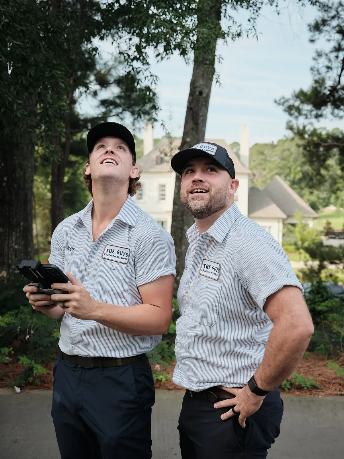 Two uniformed exterior cleaning technicians looking up at a home's roofline, assessing the work ahead
